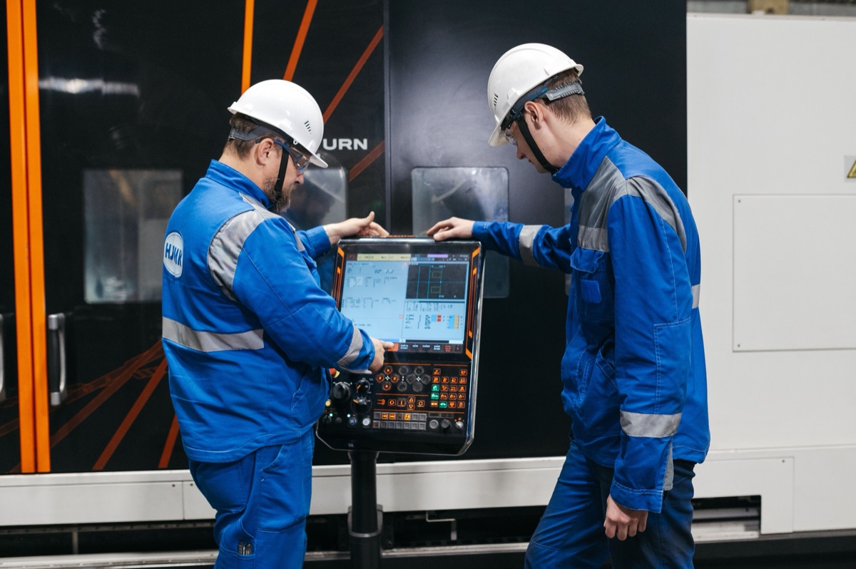 Two machine operators reviewing a CNC control panel